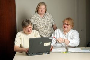 Drei ältere Damen sitzen vor einem Aktenordner und einem Laptop.