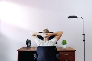 Ein Mann sitz mit hinterm Kopf verschränkten Armen an einem Schreibtisch.