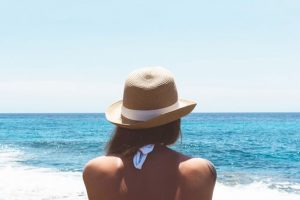 Dame mit Bikini und Strandhut schaut auf das Meer.