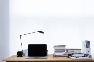 Ein Schreibtisch mit Lampe, Laptop, Büschern und Schreibutensilien.