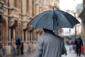 Ein Herr mit Regenschirm überquerrt eine Straße nei Regen