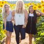 Drei Freundinnen in einem Sonnenblumenfeld lachen in die Kamera.