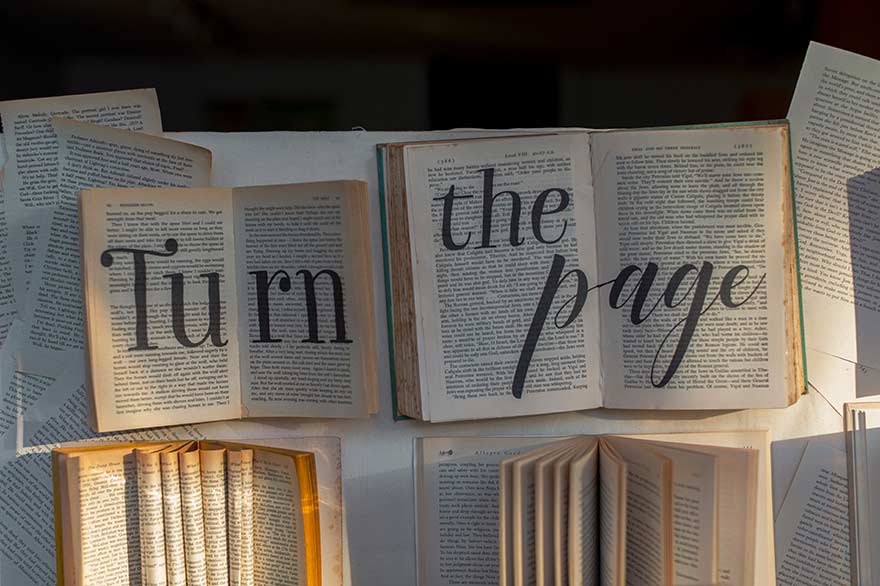 Aufgeschlagene Bücher, auf die übergroß geschrieben ist "Turn the page".