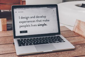 Aufgeklappter Laptop auf einem Holztisch zeigt den Satz "I design and develop experiences that make people´s lives simple."