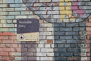 Bunt bemalte Steinwand, Schild "Accessible Entry" mit Rollstuhl-Symbol