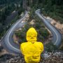 Eine PErson mit einer gelben Kapuzenjacke sitzt auf einem Berg und schaut herab auf eine gewundene Straße