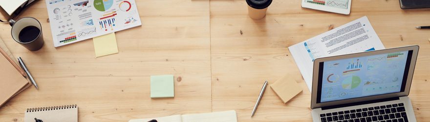 Tisch von oben mit mehreren Schreibutensilien, Laptop und einigen Geschäftsleuten.