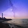 Nachthimmel über einem Leuchtturm am Meer.